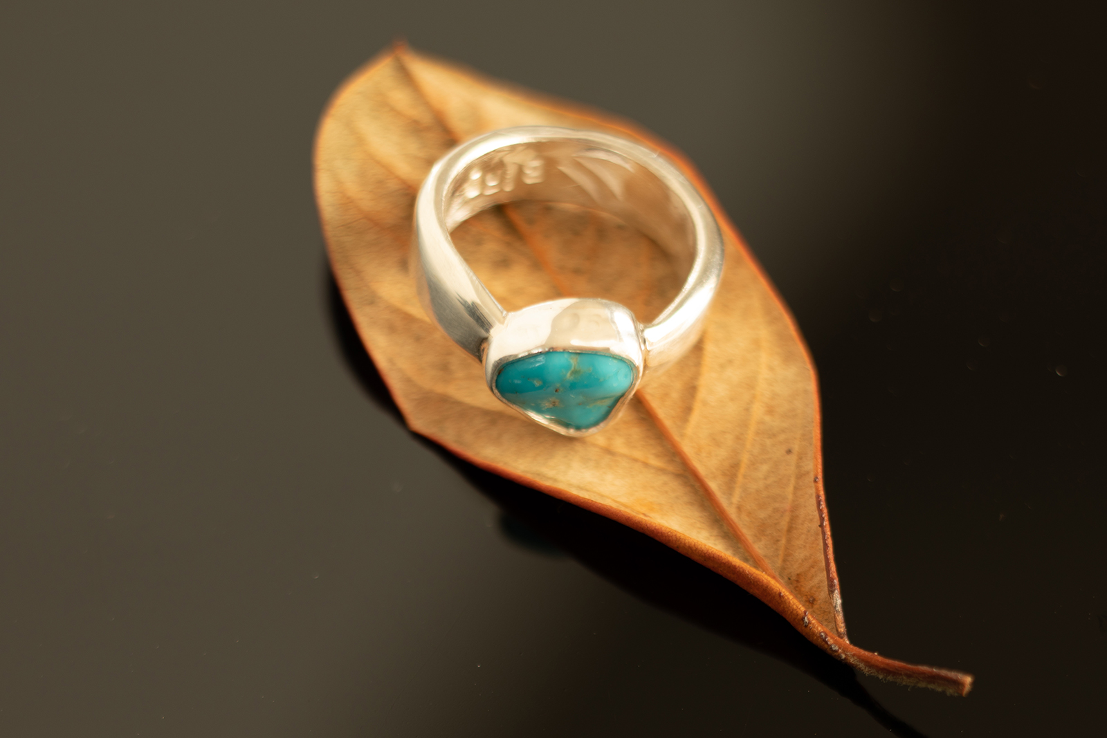 Ring on dark table on brown leaf.