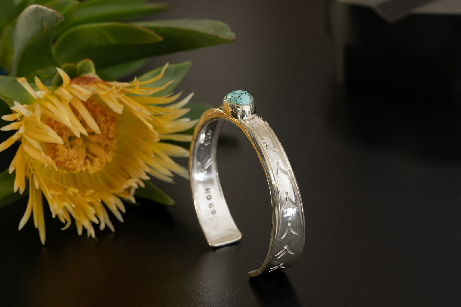 Yellow flower and silver cuff on dark table.